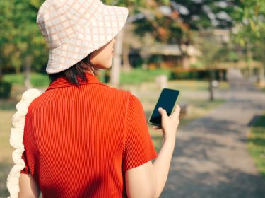 Eine Frau geht spazieren und hält dabei ihr Smartphone in der Hand.