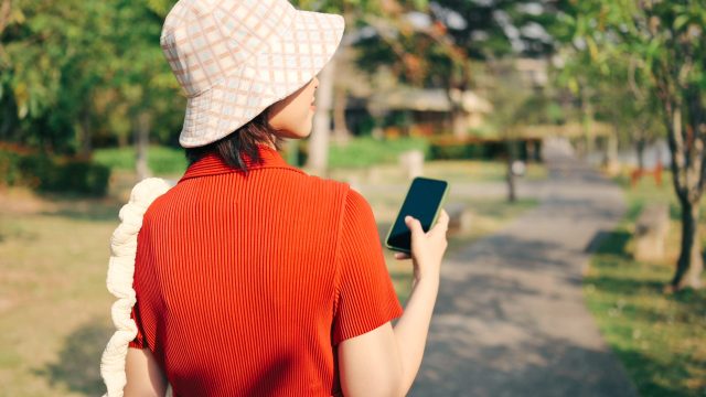 Eine Frau geht spazieren und hält dabei ihr Smartphone in der Hand.