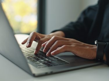 Auf dem Bild mit symbolischem Bezug zu Perplexity Pro ist eine Person in Business-Kleidung zu sehen, die konzentriert auf einem modernen Laptop tippt. Die Szene wirkt professionell und fokussiert, im Hintergrund ist ein Fenster mit natürlichem Licht und unscharfem Ausblick zu erkennen. Am Handgelenk trägt die Person eine Smartwatch.