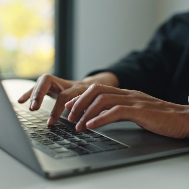 Auf dem Bild mit symbolischem Bezug zu Perplexity Pro ist eine Person in Business-Kleidung zu sehen, die konzentriert auf einem modernen Laptop tippt. Die Szene wirkt professionell und fokussiert, im Hintergrund ist ein Fenster mit natürlichem Licht und unscharfem Ausblick zu erkennen. Am Handgelenk trägt die Person eine Smartwatch.