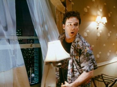 Filmszene aus Zimmer 1408: Mike Enslin (John Cusack) steht mit einer Lampe in der Hand vor dem geöffneten Fenster und schaut sich ängstlich um.