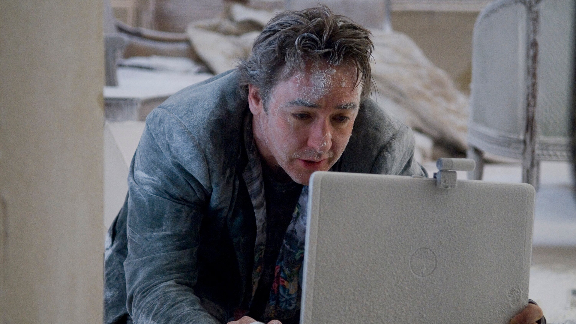 Mike (John Cusack) ist mit Asche überzogen und schaut in sein Notebook.