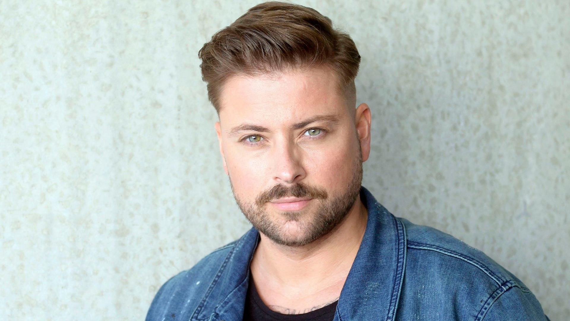 Auf diesem Porträt zur GZSZ-Besetzung ist Felix von Jascheroff zu sehen. Er trägt eine Jeansjacke über einem schwarzen Shirt und schaut in die Kamera.