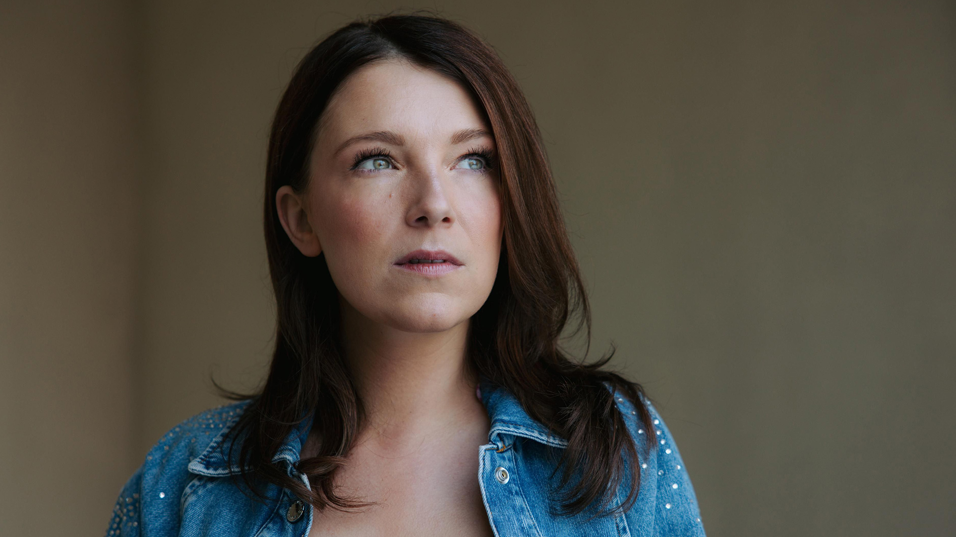 Das Bild zur GZSZ-Besetzung zeigt Iris Mareike Steen. Sie trägt eine Jeansjacke mit kleinen Glitzersteinen und blickt zur Seite.