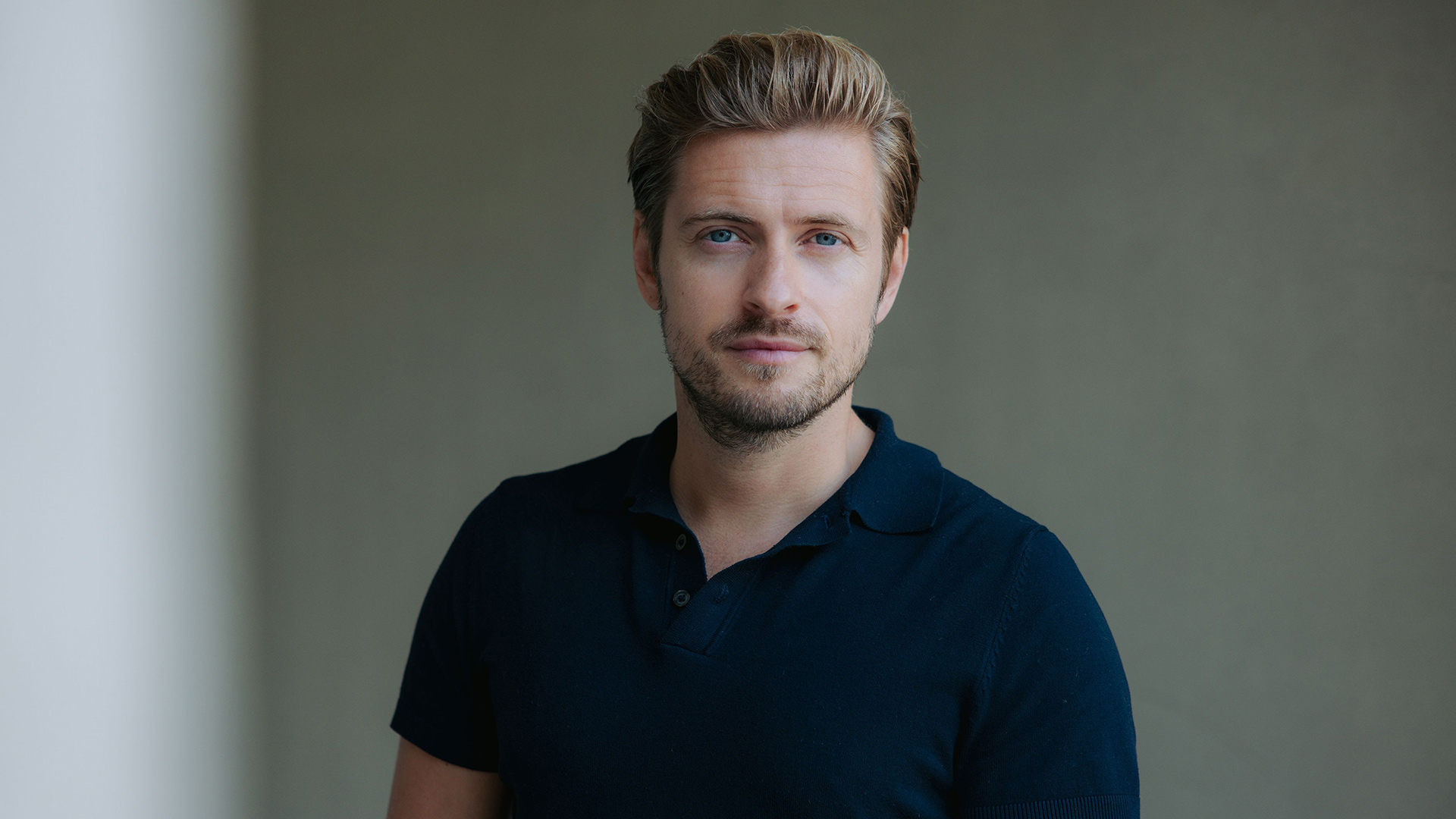 Jörn Schlönvoigt ist auf diesem Bild zur GZSZ-Besetzung zu sehen. Er trägt ein dunkelblaues Poloshirt und schaut in die Kamera.