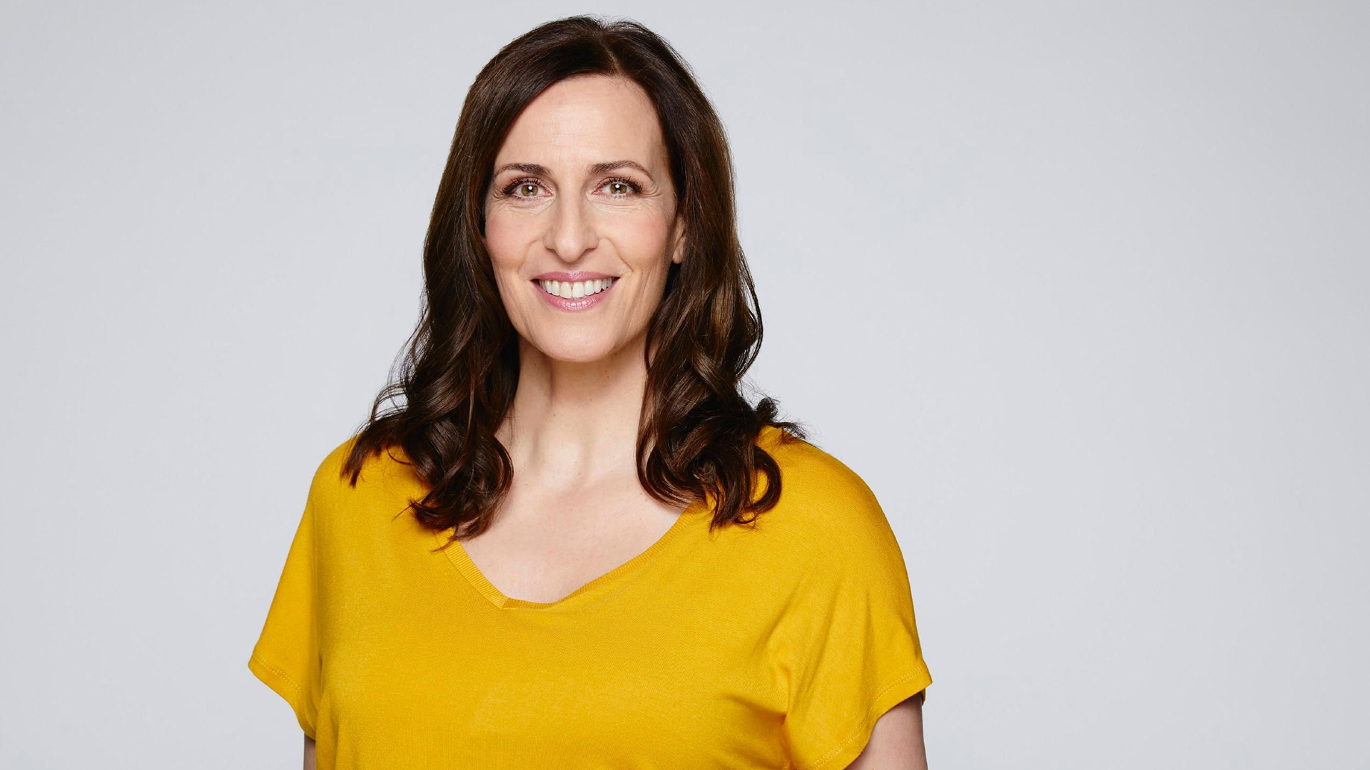 Auf diesem Bild zur GZSZ-Besetzung ist Ulrike Frank zu sehen. Sie trägt ein gelbes Oberteil und lächelt in die Kamera.