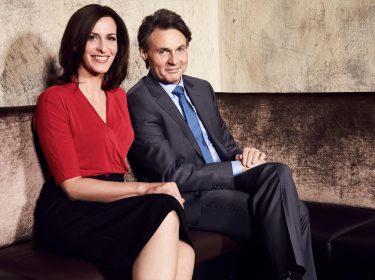 Auf dem Bild zur GZSZ-Besetzung sitzen Ulrike Frank und Wolfgang Bahro nebeneinander auf einem Sofa. Ulrike Frank trägt eine rote Bluse, Wolfgang Bahro einen grauen Anzug.