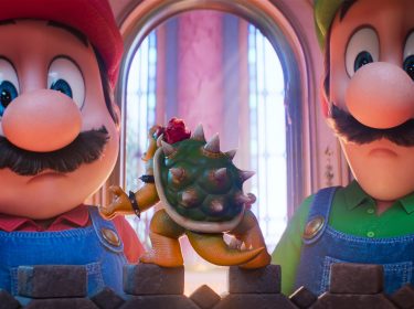 In dieser Szene aus Der Super Mario Galaxy Film stehen Mario, gesprochen von Chris Pratt, und Luigi, gesprochen von Charlie Day, vor einer kleinen Bowser-Figur, deren Filmversion von Jack Black gesprochen wird. Beide Brüder blicken überrascht auf das Mini-Modell, während warmes Schlosslicht durch hohe Fenster fällt und die Situation humorvoll wirken lässt.