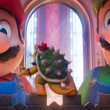 In dieser Szene aus Der Super Mario Galaxy Film stehen Mario, gesprochen von Chris Pratt, und Luigi, gesprochen von Charlie Day, vor einer kleinen Bowser-Figur, deren Filmversion von Jack Black gesprochen wird. Beide Brüder blicken überrascht auf das Mini-Modell, während warmes Schlosslicht durch hohe Fenster fällt und die Situation humorvoll wirken lässt.
