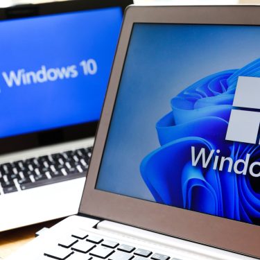 Zwei Notebooks, das im Hintergrund mit dem Logo von Windows 10, das im Vordergrund mit dem Logo von Windows 11