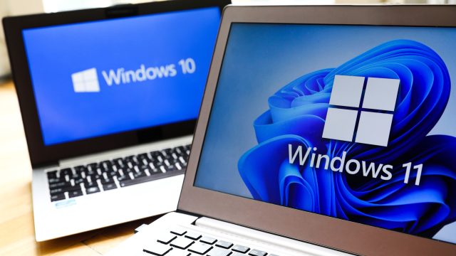 Zwei Notebooks, das im Hintergrund mit dem Logo von Windows 10, das im Vordergrund mit dem Logo von Windows 11