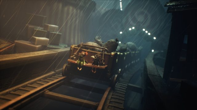 In der Szene aus dem Little Nightmares 3-Tipps-Artikel sitzen Low und Alone in einem offenen Minenwagen, der bei starkem Regen über wackelige Schienen rollt.