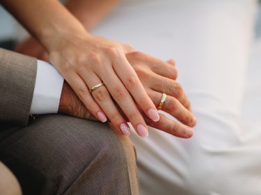 Auf dem Bild in dem Artikel zu Hochzeit auf den ersten Blick 2025 sind zwei Hände zu sehen. Beide tragen goldene Eheringe.