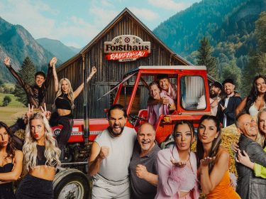 Auf dem Gruppenbild zur Show Forsthaus Rampensau Germany stehen vor einer alpinen Holzhütte zahlreiche Kandidat*innen, darunter Melina Hoch mit Max Bornmann, Eva Benetatou, Walentina Doronina, Leon.Content, Gina Beckmann, Maurice Dziwak mit Vater Frank, Yeliz Koc, Dilara Kruse, Paul Aubster, Oliver Gaukel, Christo, C-Bas, Marc Robin Wenz, Henna, Bernhard Schwendemann und Sarah Knappik. Die Stimmung ist ausgelassen und voller Vorfreude.