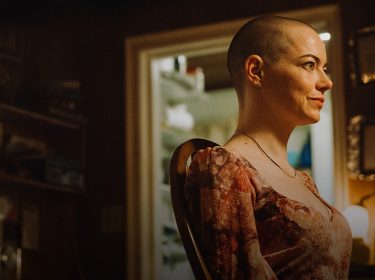 Emma Stone in Bugonia: Eine Frau mit kurz rasiertem Kopf sitzt in einem warm beleuchteten Raum und blickt entschlossen zur Seite.