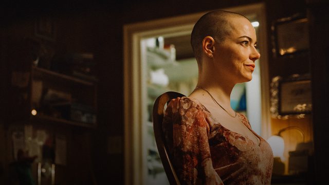 Emma Stone in Bugonia: Eine Frau mit kurz rasiertem Kopf sitzt in einem warm beleuchteten Raum und blickt entschlossen zur Seite.