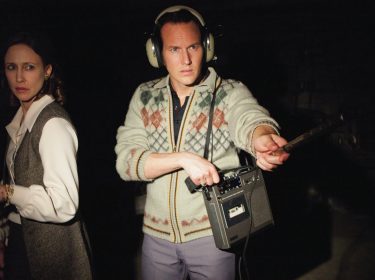 Auf dem Bild aus dem Gruselfilm Conjuring – Die Heimsuchung sind Lorraine und Ed Warren zu sehen, gespielt von Vera Farmiga und Patrick Wilson. Ed trägt Kopfhörer und hält ein Tonbandgerät in der Hand, während er konzentriert in die Dunkelheit zeigt. Lorraine blickt ernst in eine andere Richtung. Die düstere Atmosphäre verstärkt die unheimliche Stimmung typischer Gruselfilme.