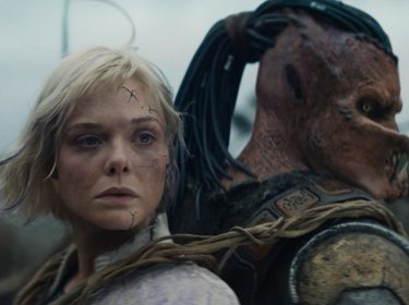 Predator: Badlands: Eine junge Frau mit blonden, zerzausten Haaren und Narben im Gesicht steht dicht neben einem furchteinflößenden außerirdischen Wesen mit gepanzerter Haut und markanten Fangzähnen.