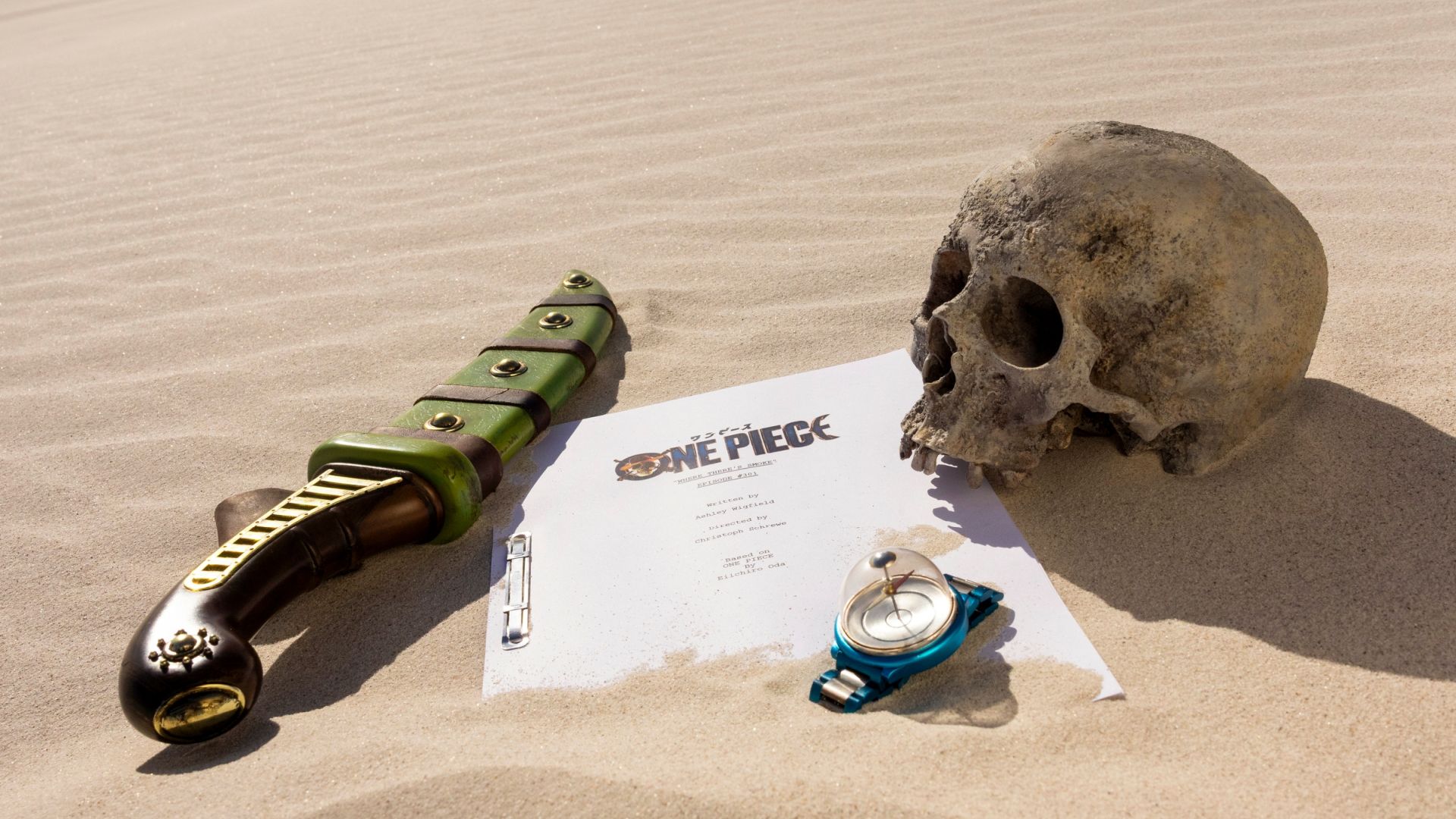 Ein Dolch, ein Skript, ein Kompass und ein Schädel liegen in der Wüste.