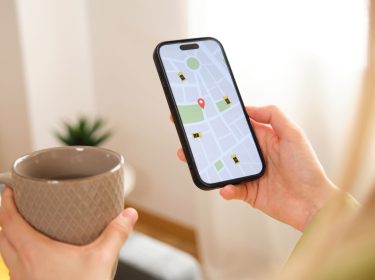 Frau mit Tasse in der Hand schaut auf die Navigations-App auf ihrem iPhone.