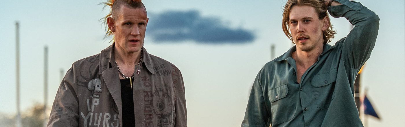 Auf dem Bild in den GigaTV-Highlights im November 2025 siehst Du eine Szene aus dem Film „Caught Stealing“. Austin Butler und Matt Smith laufen nebeneinander. Smith trägt eine auffällige Jacke mit Punk-Schriftzügen und einen orange-gelben Irokesenhaarschnitt, während Butler ein grünes Hemd trägt und sich mit der Hand durch die Haare fährt.