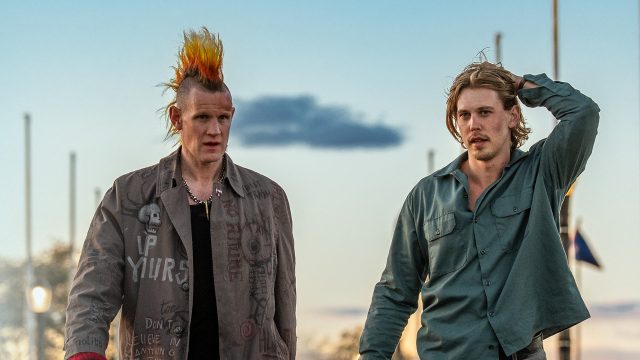 Auf dem Bild in den GigaTV-Highlights im November 2025 siehst Du eine Szene aus dem Film „Caught Stealing“. Austin Butler und Matt Smith laufen nebeneinander. Smith trägt eine auffällige Jacke mit Punk-Schriftzügen und einen orange-gelben Irokesenhaarschnitt, während Butler ein grünes Hemd trägt und sich mit der Hand durch die Haare fährt.