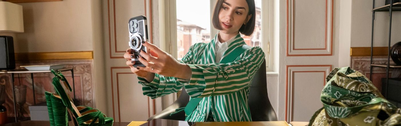 In den Streaming-Highlights im Dezember 2025 siehst du Lily Collins als Emily in der 5 Staffel von „Emily in Paris“. Sie sitzt an einem Schreibtisch und macht ein Selfie.