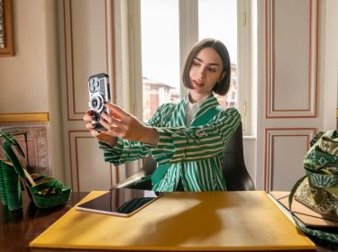 In den Streaming-Highlights im Dezember 2025 siehst du Lily Collins als Emily in der 5 Staffel von „Emily in Paris“. Sie sitzt an einem Schreibtisch und macht ein Selfie.