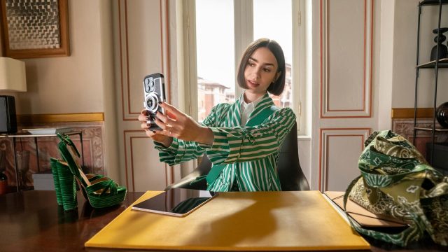 In den Streaming-Highlights im Dezember 2025 siehst du Lily Collins als Emily in der 5 Staffel von „Emily in Paris“. Sie sitzt an einem Schreibtisch und macht ein Selfie.