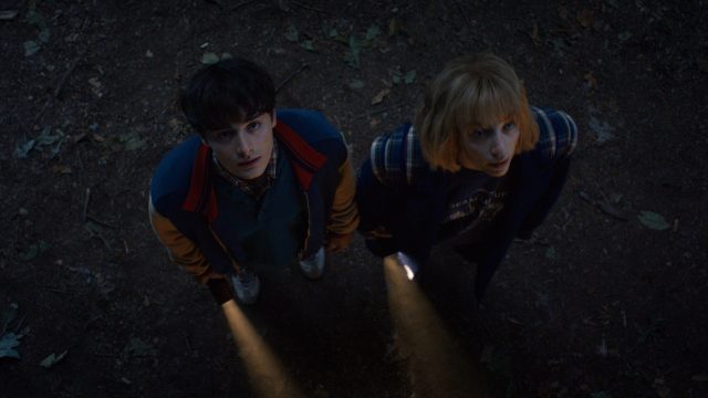 In den Streaming-Highlights im November 2025 siehst du eine Szene aus Stranger Things Staffel 5. Auf dem Bild sind Noah Schnapp als Will Byers und Maya Hawke als Robin Buckley zu sehen. Beide blicken an einem dunklen Ort mit ernster Miene nach oben, ihre Taschenlampen werfen Licht auf den Boden.