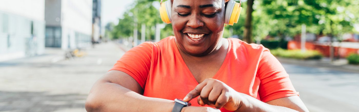 Eine Frau mit Kopfhörern bedient lächelnd ihre Apple Watch