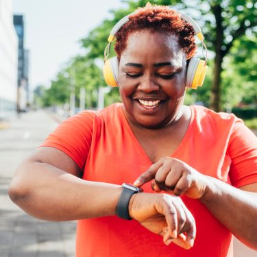 Eine Frau mit Kopfhörern bedient lächelnd ihre Apple Watch