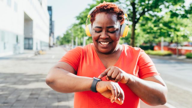 Eine Frau mit Kopfhörern bedient lächelnd ihre Apple Watch