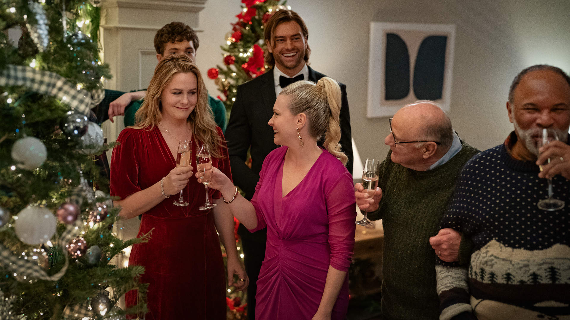 Melissa Joan Hart und Alicia Silverstone in A Merry Little Ex-Mas: Eine festlich gekleidete Gruppe stößt mit Sektgläsern vor einem geschmückten Weihnachtsbaum an; die Stimmung ist fröhlich und herzlich.