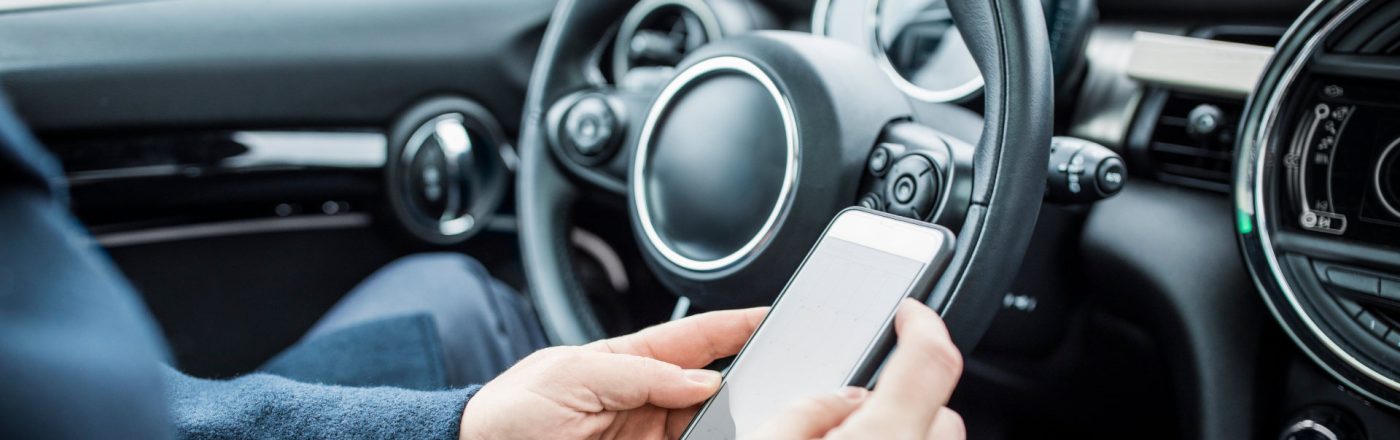 Eine Person sitzt im Auto und bedient ihr Smartphone.
