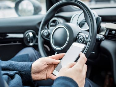 Eine Person sitzt im Auto und bedient ihr Smartphone.