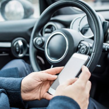 Eine Person sitzt im Auto und bedient ihr Smartphone.