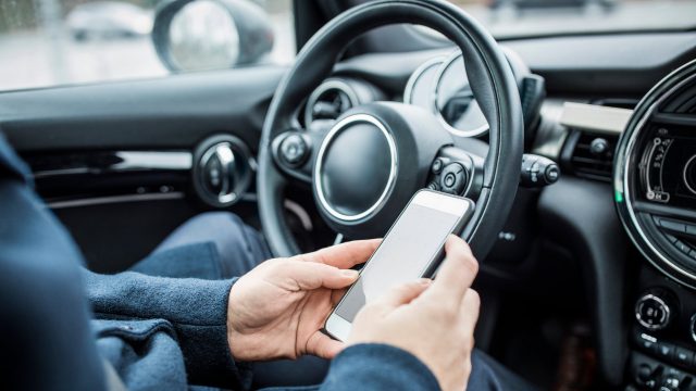 Eine Person sitzt im Auto und bedient ihr Smartphone.