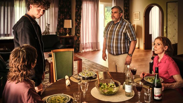 Mikes Eltern Gustav und Emilia am Tisch mit Mike und Nisha. Gustav und Mike stehen, Nisha und Emilia sitzen.