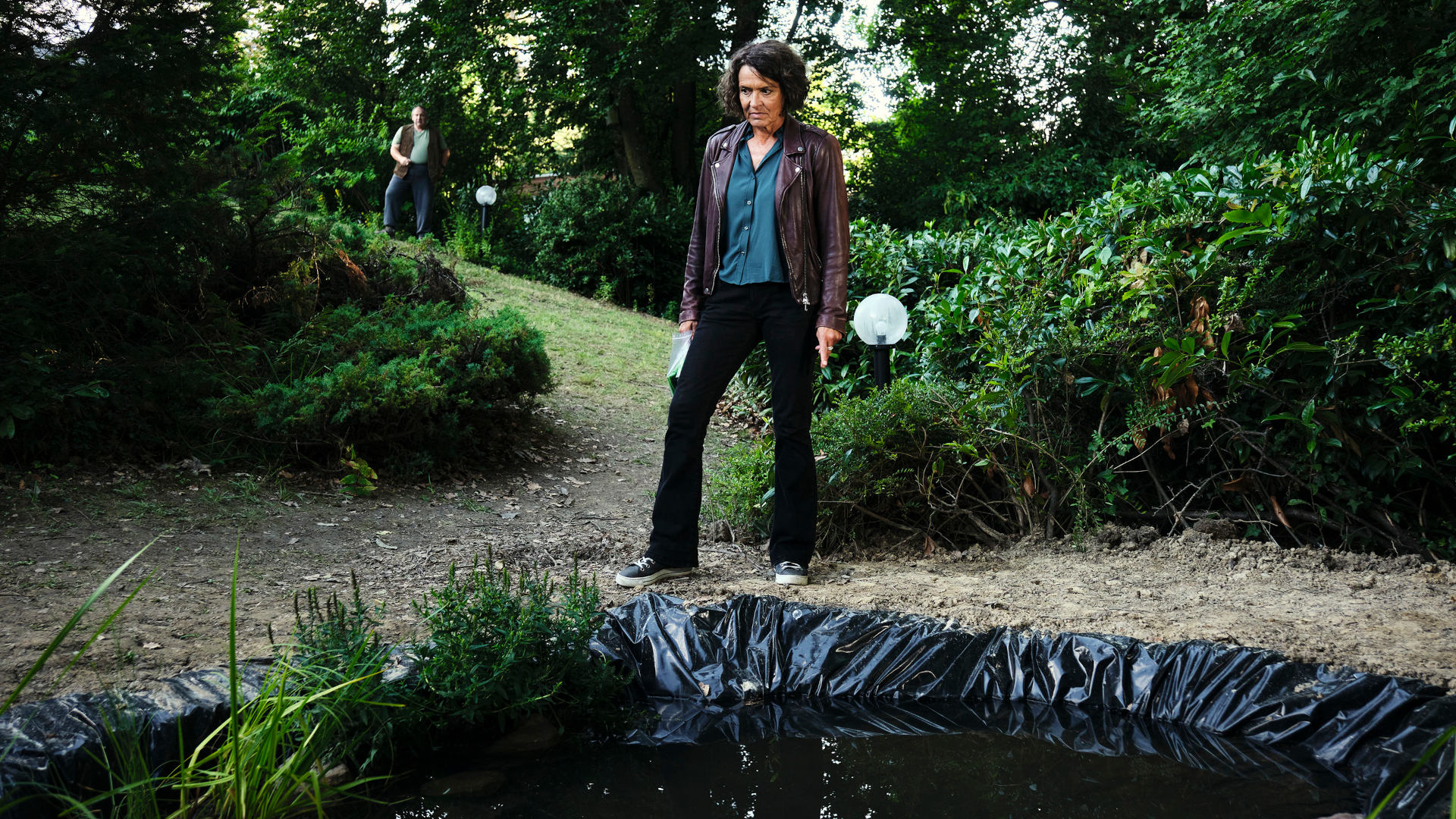 Kommissarin Lena Odenthal steht im Garten von Mikes Eltern und schaut auf den frisch angelegten Gartenteich.