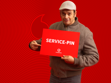 Kaya Yanar ist auf dem Bild zur Vodafone Service-PIN Kampagne zu sehen, wie er ein rotes Schild mit der Aufschrift „SERVICE-PIN“ hält und darauf zeigt.