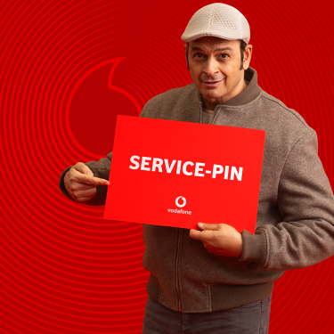 Kaya Yanar ist auf dem Bild zur Vodafone Service-PIN Kampagne zu sehen, wie er ein rotes Schild mit der Aufschrift „SERVICE-PIN“ hält und darauf zeigt.