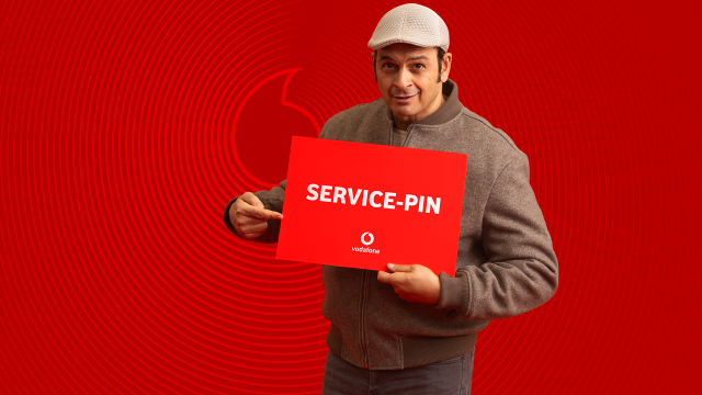 Kaya Yanar ist auf dem Bild zur Vodafone Service-PIN Kampagne zu sehen, wie er ein rotes Schild mit der Aufschrift „SERVICE-PIN“ hält und darauf zeigt.