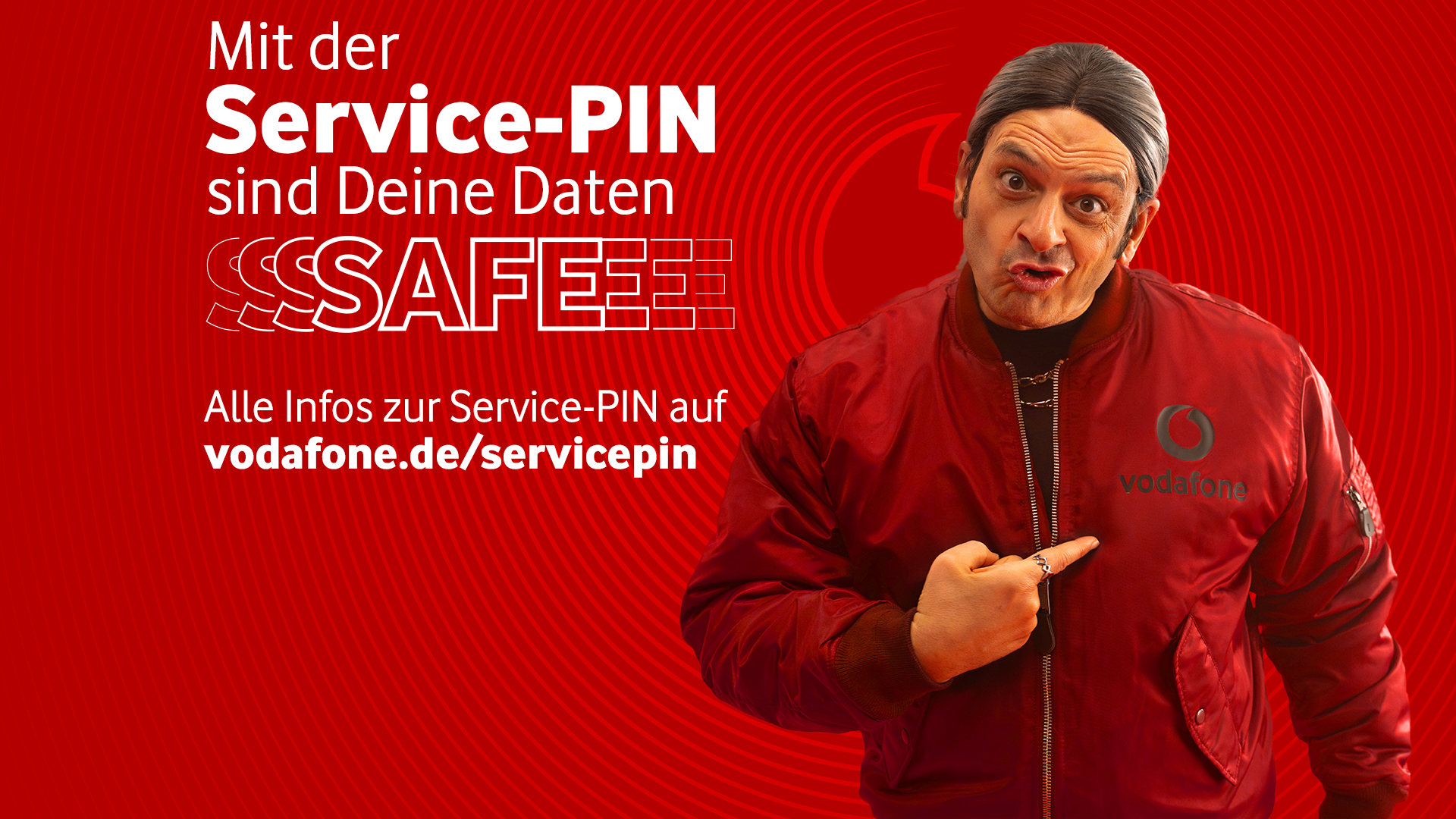 In der Vodafone Service-PIN Kampagne zeigt Kaya Yanar in roter Vodafone-Jacke mit ernstem Blick und zusammengebundenem Haar auf das Firmenlogo. Der Hintergrund ist kräftig rot mit dem Schriftzug „Mit der Service-PIN sind Deine Daten SAFEEE“.