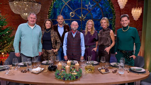 Horst Lichter, Walter Lehnertz, Wendela Horz, Julian Schmitz-Avila, Horst Lichter, Annika Raßbach, Susanne Steiger und Fabian Kahl stehen hinter einer festlich gedeckten Tafel und lächeln in die Kamera. Im Hintergrund ist ein großes geschmücktes Fenster sowie Weihnachtsdekoration zu sehen.