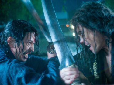 Szenenbild aus der Serie Last Samurai Standing: Zwei Kämpfer mit nassen Haaren liefern sich im strömenden Regen einen intensiven Schwertkampf, ihre Klingen blockieren sich in einem kraftvollen Schlagabtausch.