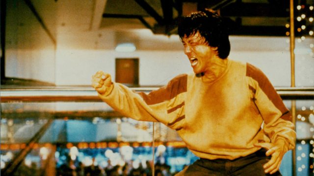 Das Bild zeigt Jackie Chan in einer ikonischen Szene aus Police Story. Schweißgebadet und voller Energie schreit er kampfbereit mit geballter Faust – typisch für seine Rolle als einer der kompromisslosesten Actionhelden der 80er und 90er. Der Hintergrund zeigt ein Einkaufszentrum, in dem gerade eine intensive Actionszene stattfindet.