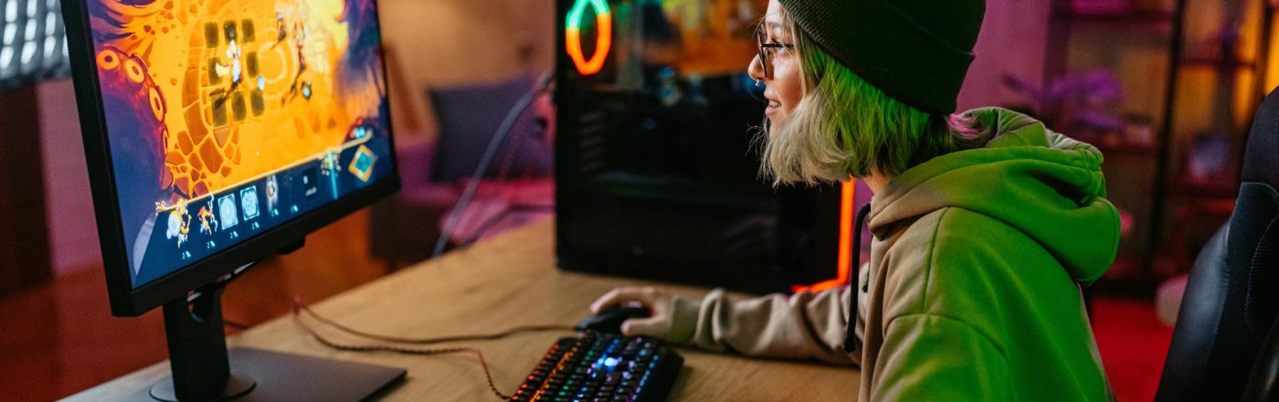 Beim Cloud-Gaming Vergleich zeigt dieses Bild eine junge Person mit grüner Mütze und Kapuzenpullover, die an einem RGB-beleuchteten Gaming-Setup spielt, während ein farbenfrohes Spiel auf dem Monitor läuft.
