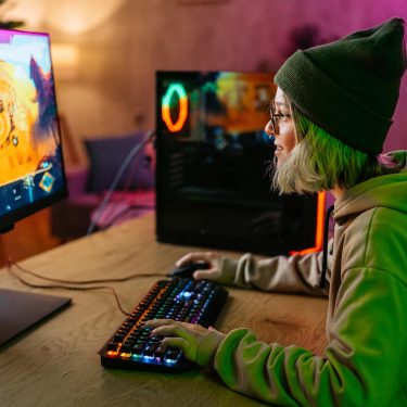 Beim Cloud-Gaming Vergleich zeigt dieses Bild eine junge Person mit grüner Mütze und Kapuzenpullover, die an einem RGB-beleuchteten Gaming-Setup spielt, während ein farbenfrohes Spiel auf dem Monitor läuft.