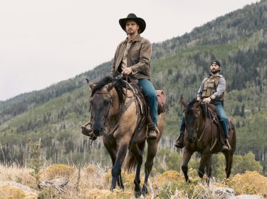 In dieser Szene aus der Marshals Serie sind Luke Grimes als Kayce Dutton und Logan Marshall-Green als Pete Calvin auf Pferden in einer bergigen, waldreichen Landschaft unterwegs. Beide tragen lässige Westernkleidung mit ernsten Gesichtsausdrücken. Die Stimmung wirkt ruhig, aber gespannt – typisch für ein modernes Western-Drama.